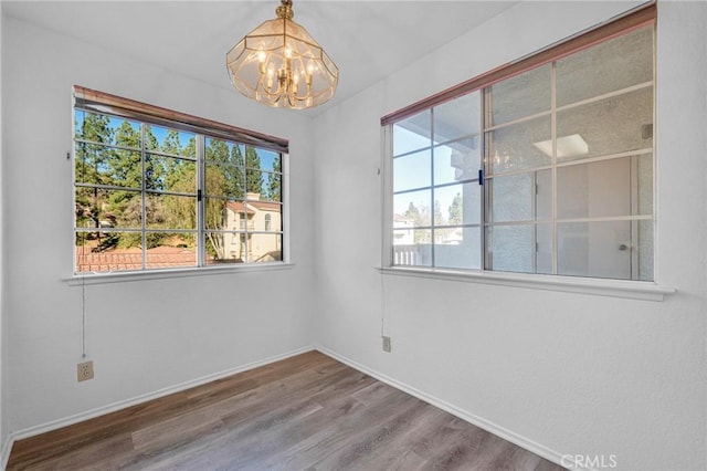 spare room featuring a notable chandelier, baseboards, and wood finished floors