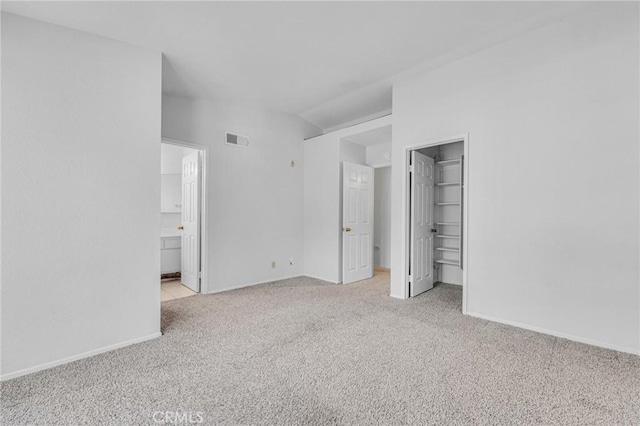 unfurnished bedroom featuring visible vents, baseboards, carpet, a walk in closet, and vaulted ceiling