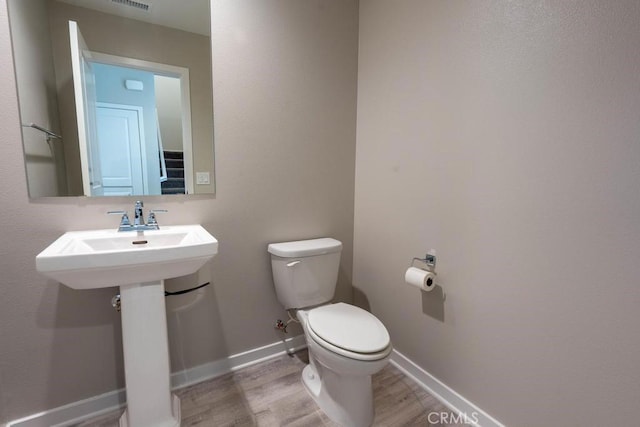 half bathroom with baseboards, visible vents, toilet, and wood finished floors