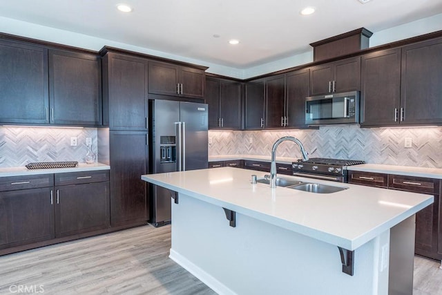 kitchen with premium appliances, a sink, light wood-style flooring, and a kitchen bar