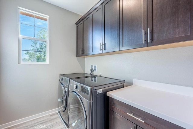 laundry room featuring cabinet space, light wood-style flooring, baseboards, and washing machine and clothes dryer