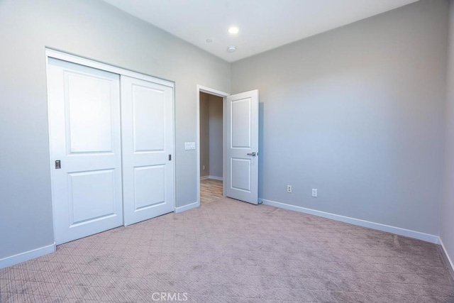 unfurnished bedroom with a closet, light carpet, and baseboards