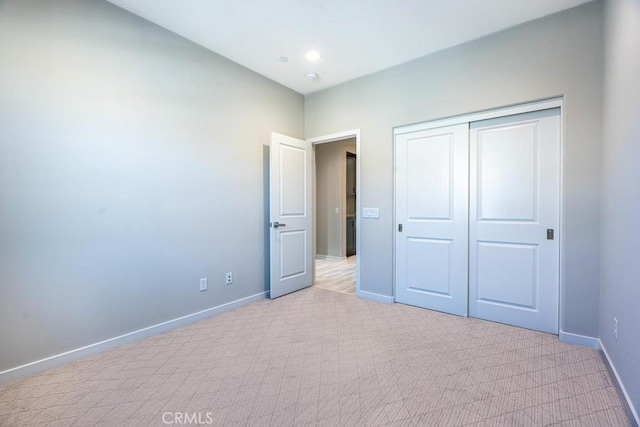 unfurnished bedroom featuring a closet, light colored carpet, and baseboards