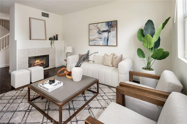 living area featuring a tile fireplace, visible vents, baseboards, and wood finished floors