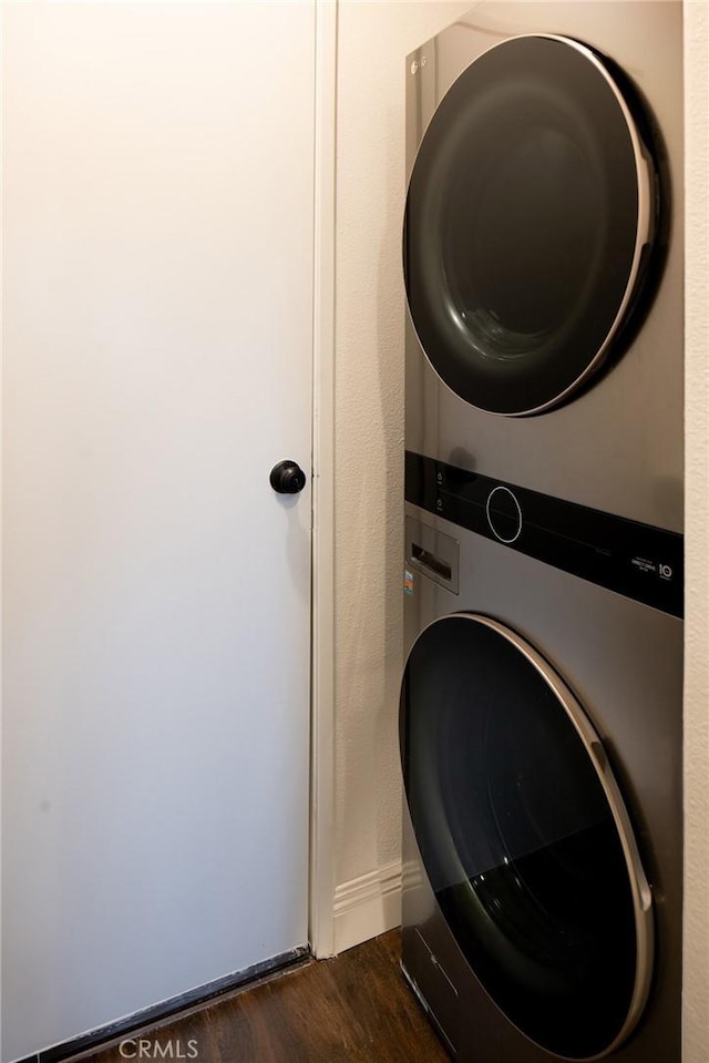 laundry room with laundry area, baseboards, dark wood finished floors, and stacked washer / dryer