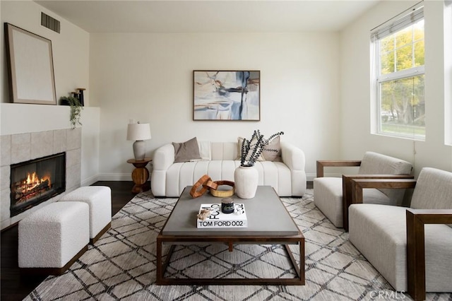 living room featuring light wood finished floors, a tile fireplace, visible vents, and baseboards