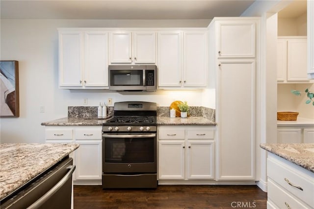 kitchen featuring appliances with stainless steel finishes, white cabinets, light stone counters, and dark wood-type flooring