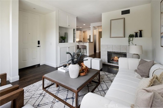 living room with dark wood-style flooring, visible vents, baseboards, and a tiled fireplace