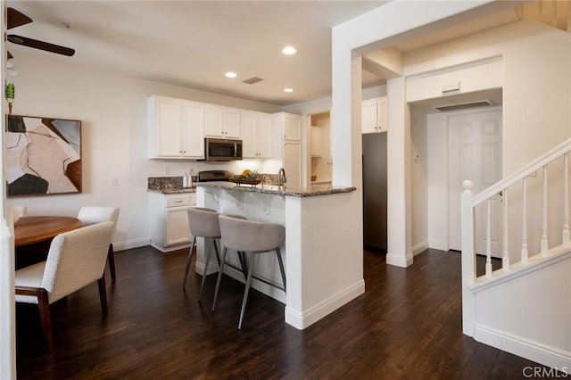 kitchen featuring recessed lighting, stainless steel appliances, dark wood-type flooring, white cabinetry, and dark stone countertops