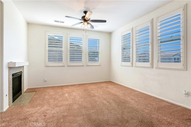 unfurnished living room with baseboards, visible vents, a ceiling fan, a fireplace with flush hearth, and carpet