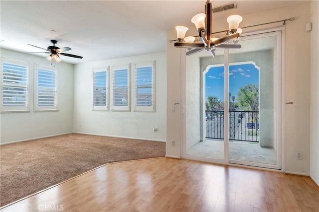 carpeted empty room with baseboards, visible vents, wood finished floors, and ceiling fan with notable chandelier