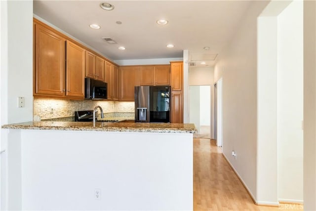 kitchen featuring a peninsula, a sink, visible vents, appliances with stainless steel finishes, and light stone countertops