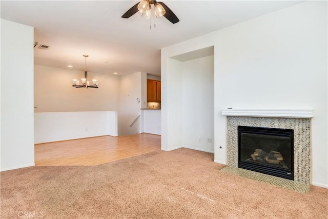 unfurnished living room featuring ceiling fan with notable chandelier, a fireplace, carpet flooring, and visible vents