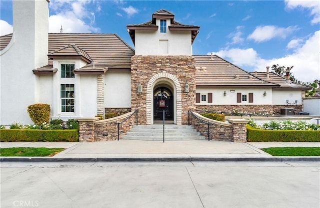 view of front facade featuring stone siding, central AC, a chimney, and stucco siding