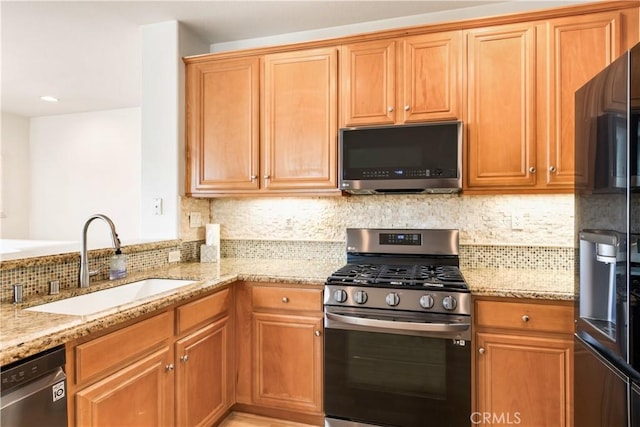 kitchen with appliances with stainless steel finishes, backsplash, a sink, and light stone countertops