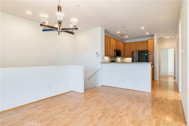 kitchen with black microwave, refrigerator with ice dispenser, light wood-type flooring, decorative backsplash, and an inviting chandelier