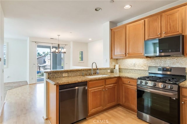 kitchen with light wood finished floors, decorative backsplash, appliances with stainless steel finishes, a sink, and light stone countertops