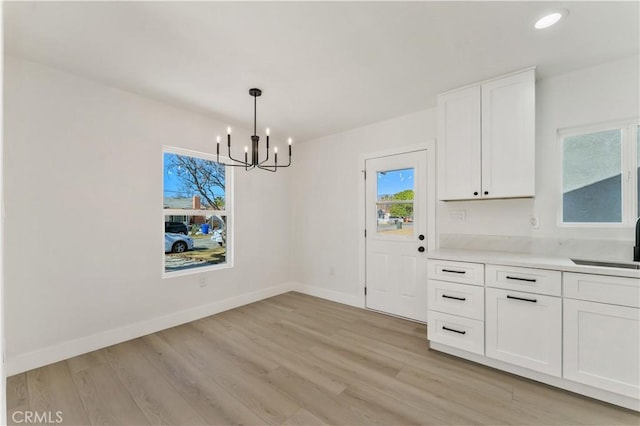 unfurnished dining area featuring recessed lighting, light wood-style flooring, an inviting chandelier, a sink, and baseboards