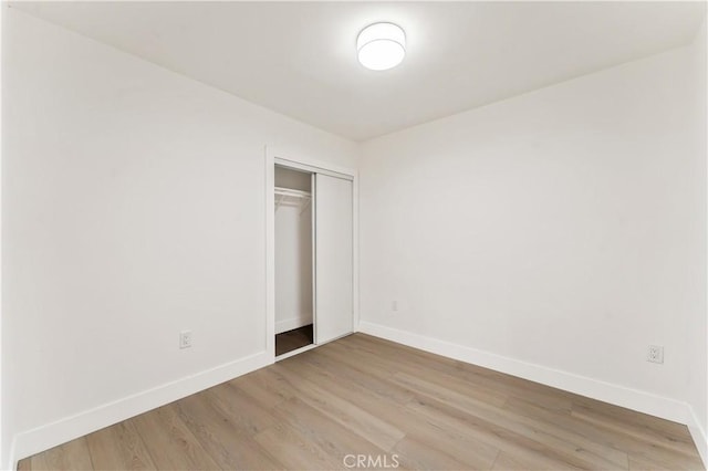 unfurnished bedroom featuring light wood-style floors, baseboards, and a closet