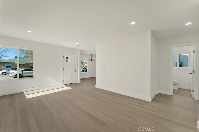 unfurnished living room featuring baseboards, light wood-type flooring, a chandelier, and recessed lighting