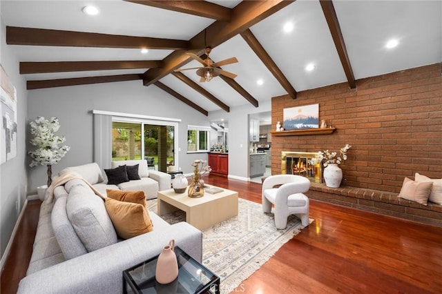 living room with a brick fireplace, vaulted ceiling with beams, wood finished floors, and baseboards