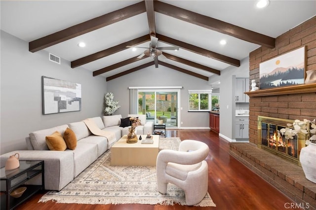 living room featuring visible vents, lofted ceiling with beams, dark wood finished floors, baseboards, and a brick fireplace