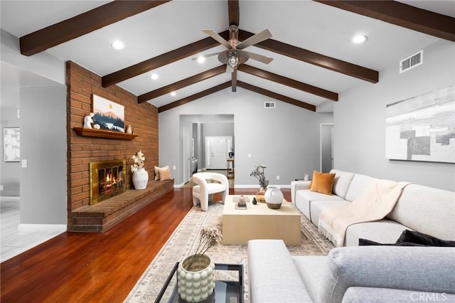 living room featuring a brick fireplace, vaulted ceiling with beams, wood finished floors, and visible vents