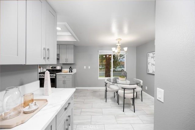 kitchen with gray cabinetry, an inviting chandelier, baseboards, stainless steel gas range, and light stone countertops