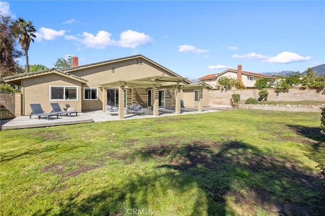 rear view of property featuring stucco siding, a lawn, a deck, fence, and a chimney