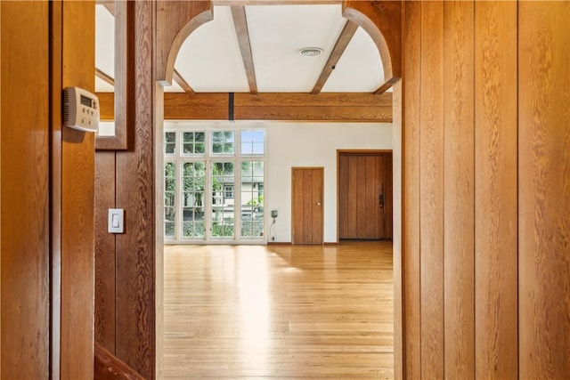 empty room featuring arched walkways, beamed ceiling, wood finished floors, and visible vents