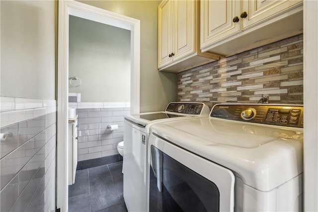 clothes washing area with laundry area, wainscoting, dark tile patterned flooring, washing machine and dryer, and tile walls