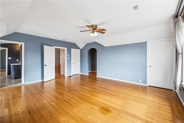 interior space featuring light wood finished floors, baseboards, arched walkways, a ceiling fan, and lofted ceiling