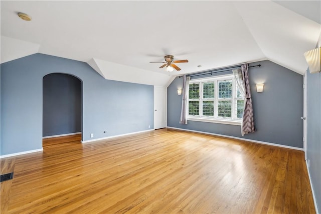 interior space with light wood-type flooring, vaulted ceiling, arched walkways, and baseboards