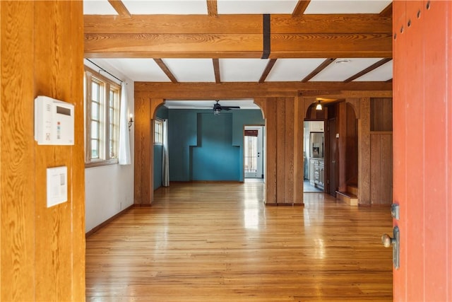 unfurnished room with wood walls, arched walkways, light wood-style floors, and beam ceiling