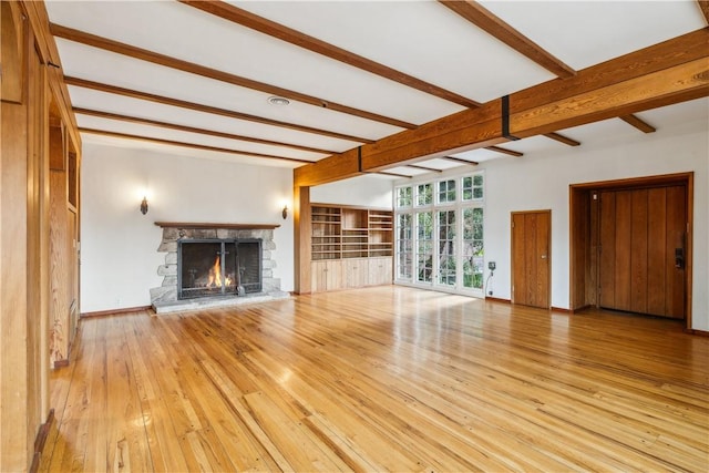 unfurnished living room with a stone fireplace, wood-type flooring, beam ceiling, and baseboards