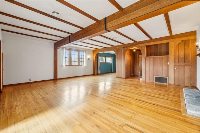 unfurnished living room with arched walkways, beam ceiling, visible vents, and light wood finished floors