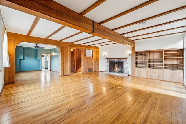 unfurnished living room with stairs, beam ceiling, a warm lit fireplace, and hardwood / wood-style flooring