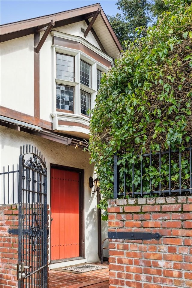 doorway to property featuring brick siding, fence, and stucco siding