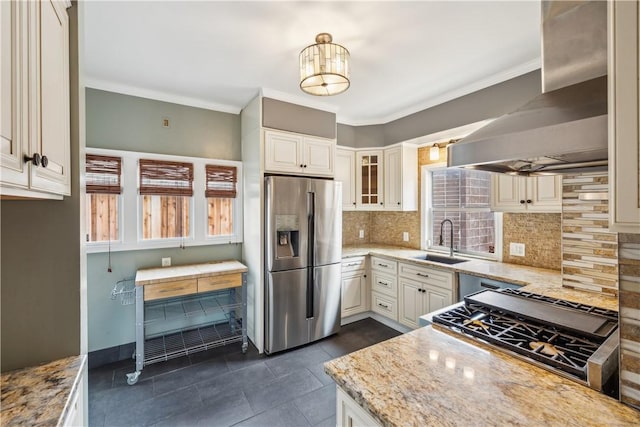 kitchen with light stone countertops, wall chimney range hood, stainless steel fridge, and a sink