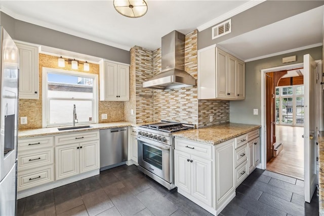 kitchen with wall chimney exhaust hood, appliances with stainless steel finishes, light stone counters, ornamental molding, and a sink