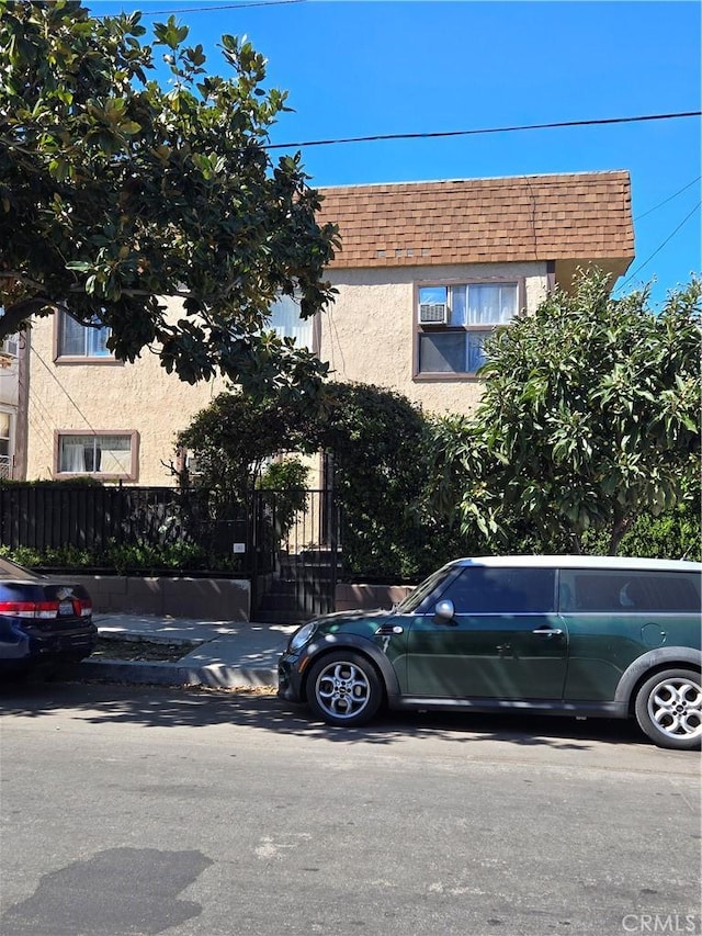 townhome / multi-family property featuring mansard roof, roof with shingles, and stucco siding