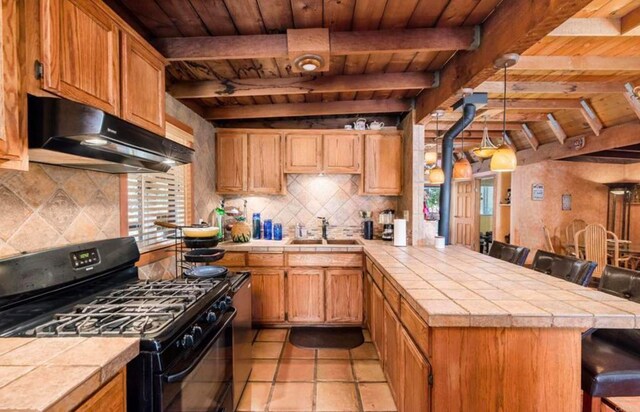 kitchen featuring a sink, under cabinet range hood, black range with gas stovetop, and tile counters