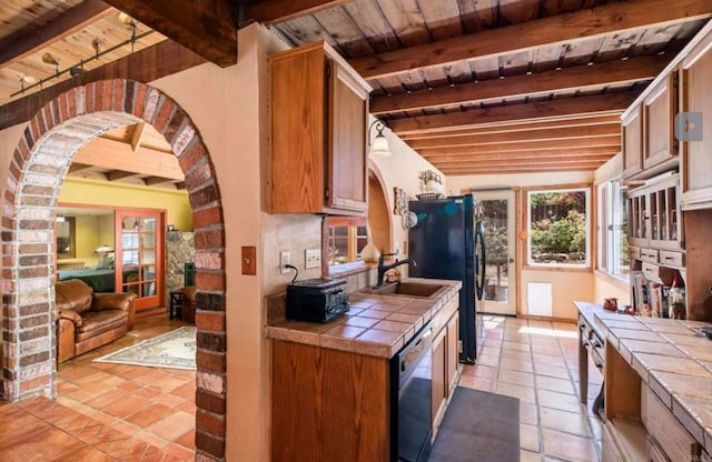 kitchen featuring arched walkways, black appliances, and tile counters