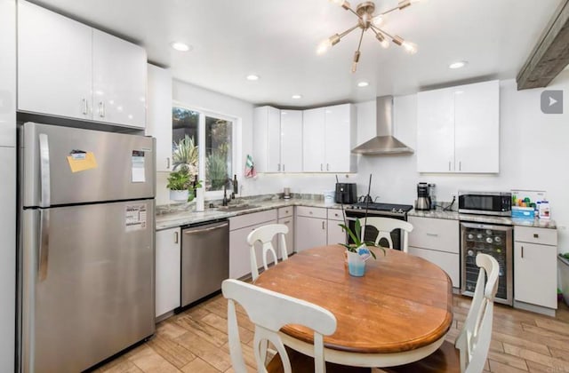 kitchen featuring light wood finished floors, wine cooler, stainless steel appliances, wall chimney range hood, and a sink