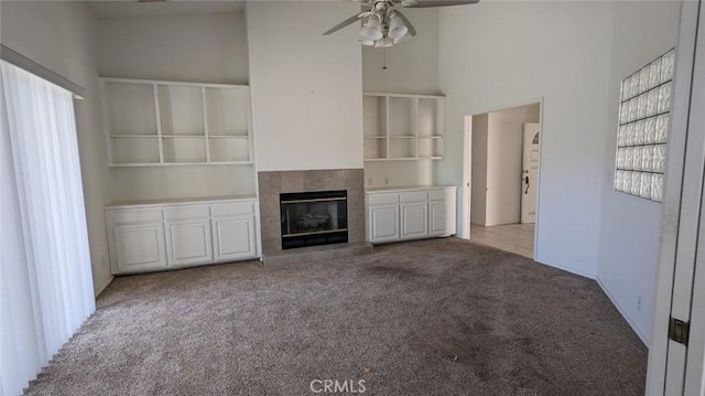 unfurnished living room featuring a towering ceiling, ceiling fan, carpet flooring, and a tile fireplace