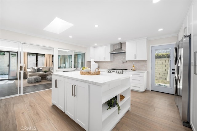 kitchen featuring wall chimney range hood, light wood-style flooring, a skylight, and freestanding refrigerator