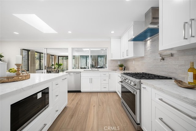 kitchen with stainless steel appliances, wall chimney range hood, a sink, and light stone countertops