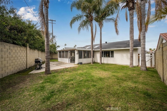 rear view of house with a sunroom, a patio area, a yard, a fenced backyard, and stucco siding