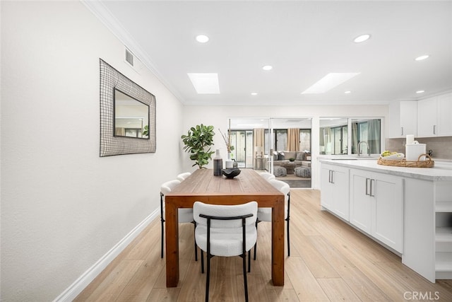 dining area featuring a skylight, crown molding, and light wood finished floors