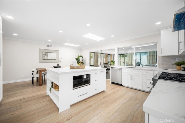 kitchen featuring stainless steel dishwasher, a sink, black microwave, a center island, and light wood finished floors